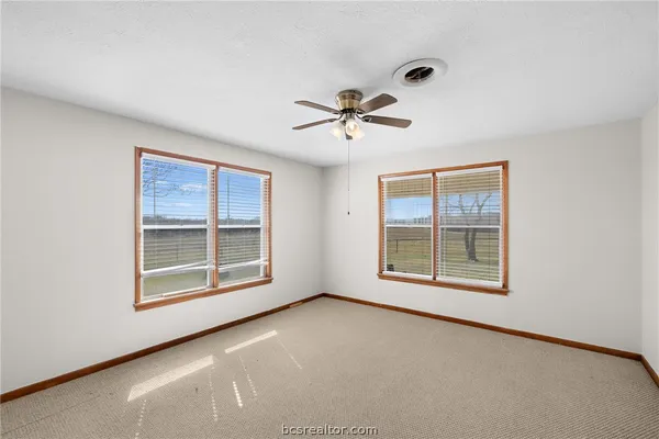 an empty room with chandelier fan and windows