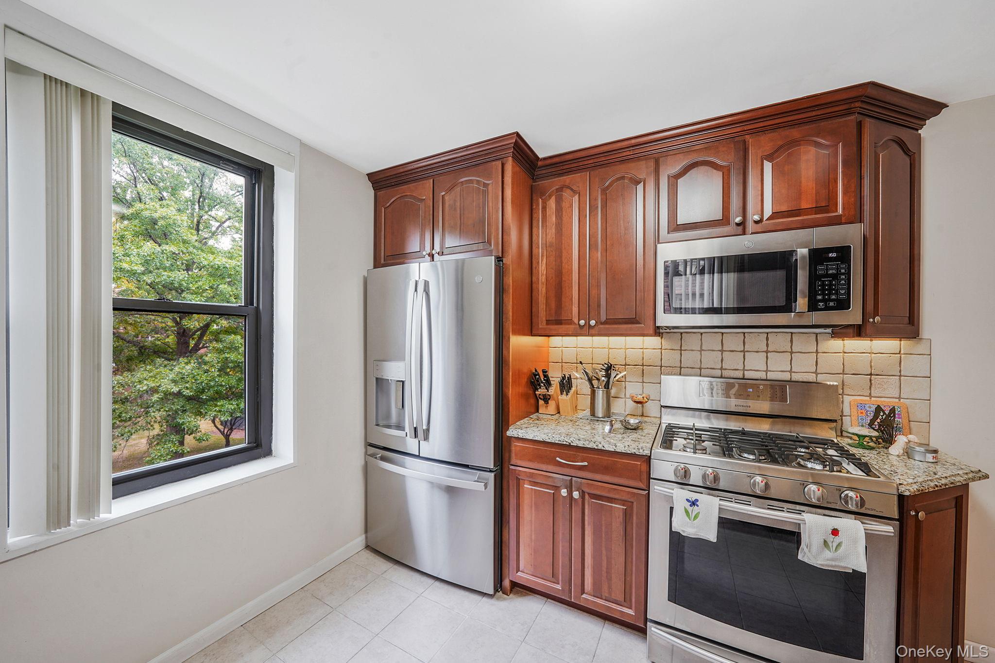18-35 Corporal Kennedy Street, Unit 2B Queens, NY 11360 - Photo 5 of 25 a kitchen with stainless steel appliances granite countertop a stove top oven a refrigerator and a sink with wooden cabinets