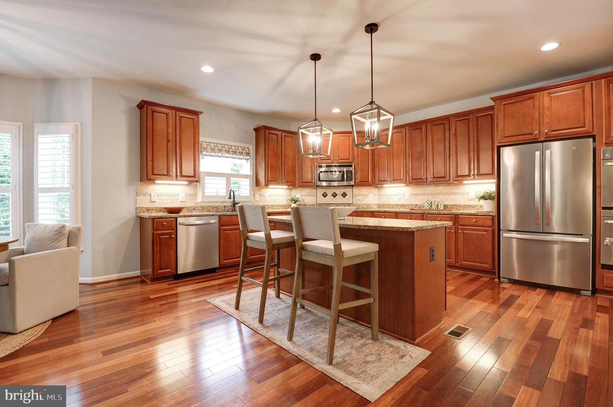 23372 Minerva Drive Brambleton, VA 20148 - Photo 12 of 61 a kitchen with stainless steel appliances granite countertop a refrigerator a sink dishwasher a dining table and chairs with wooden floor