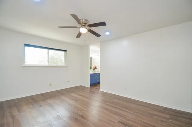 an empty room with wooden floor fan and windows