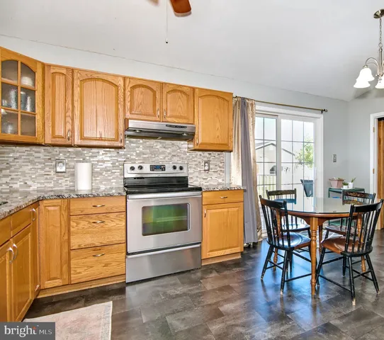 a kitchen with stainless steel appliances granite countertop wooden cabinets a dining table and chairs a refrigerator with wooden floors