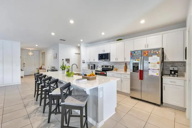 a kitchen with stainless steel appliances kitchen island granite countertop a refrigerator and a stove top oven with white cabinets
