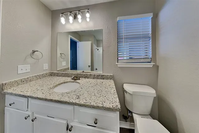 a bathroom with a granite countertop toilet a sink and mirror