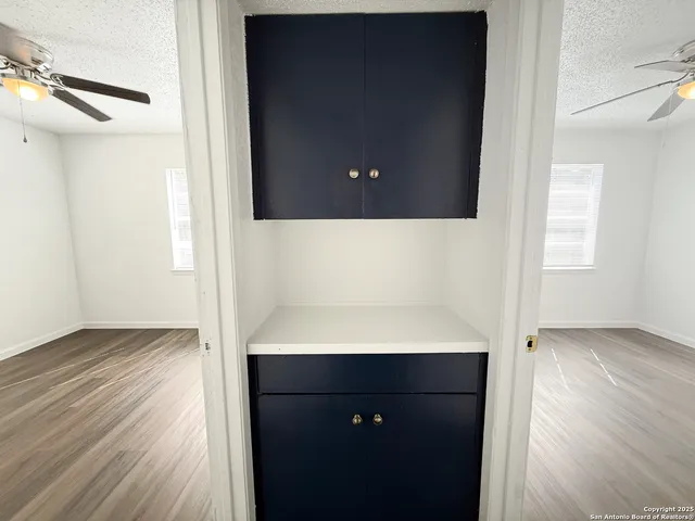a view of an empty room with wooden floor and a ceiling fan