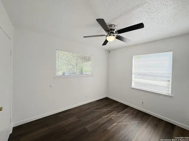 an empty room with wooden floor fan and windows