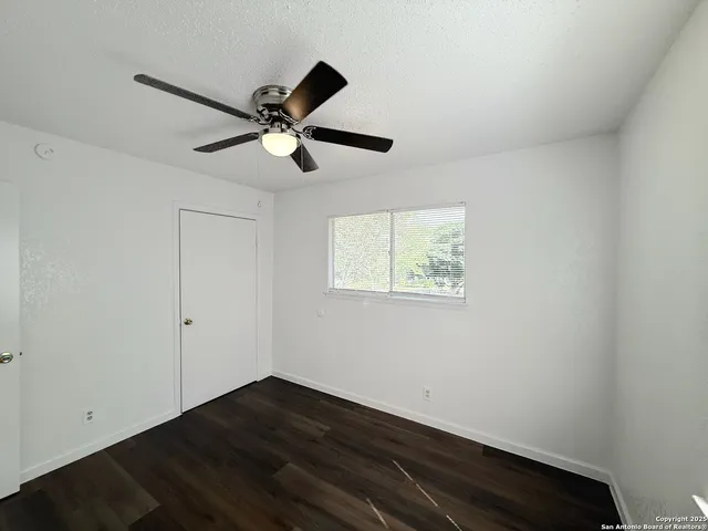 an empty room with wooden floor ceiling fan and window