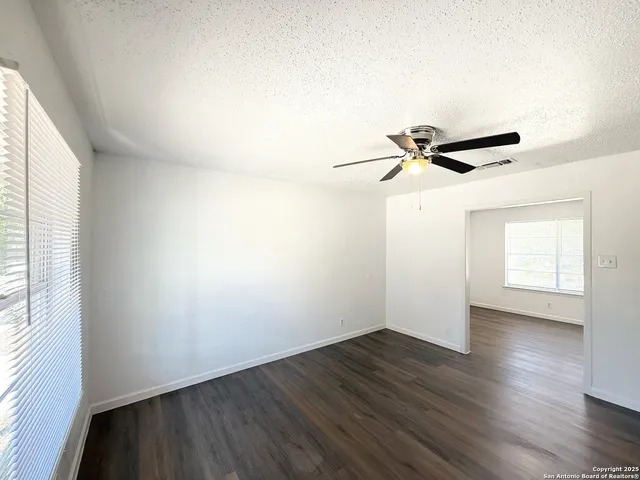 an empty room with wooden floor fan and windows