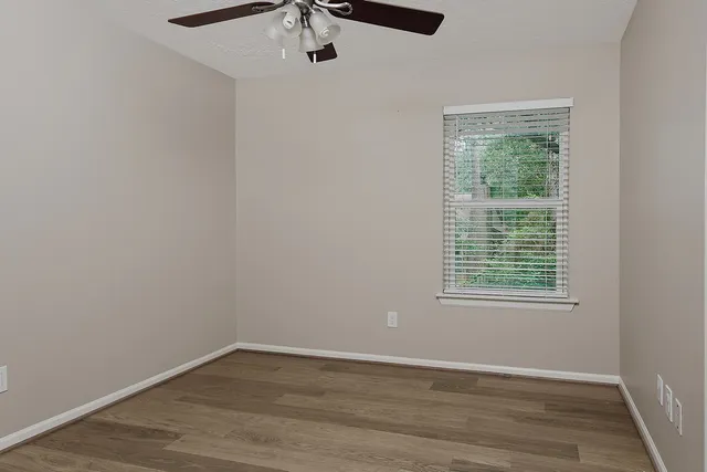 an empty room with wooden floor fan and windows