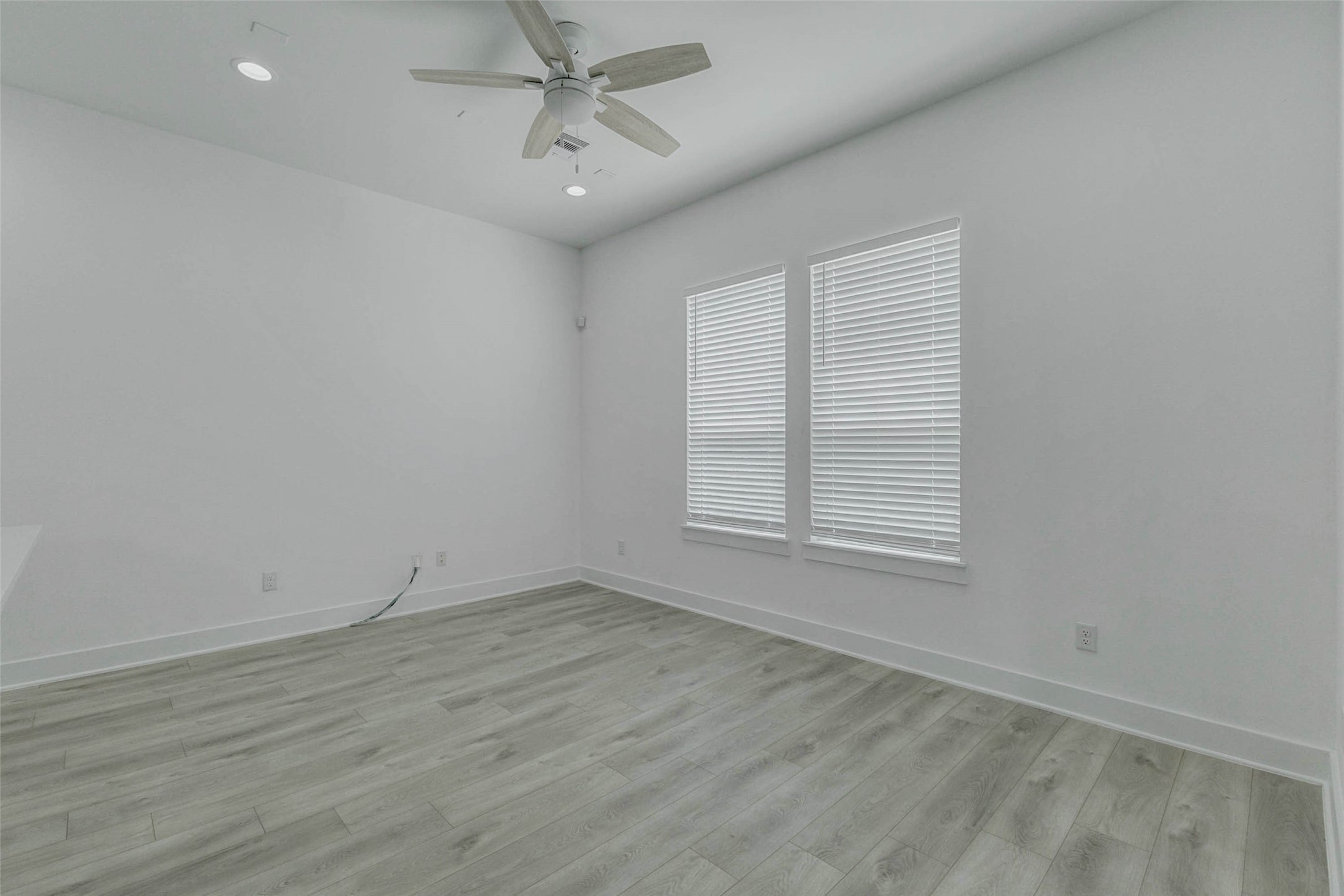 5705 Elysium Street Houston, TX 77091 - Photo 12 of 22 Spacious living room view with two large windows, white blinds, tall ceilings, ceiling fan, recessed lighting, and light wood-look floors. The neutral palette keeps the space fresh and inviting, while the open layout provides excellent flexibility for furniture placement, dining, lounging, or entertaining.
