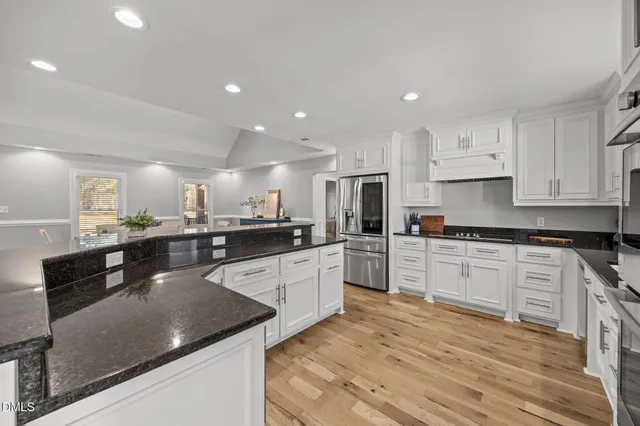 a large kitchen with stainless steel appliances granite countertop a stove a sink a refrigerator and white cabinets with wooden floor