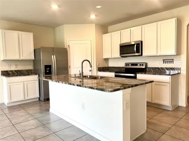 a kitchen with stainless steel appliances granite countertop a stove top oven a sink a refrigerator and white cabinets