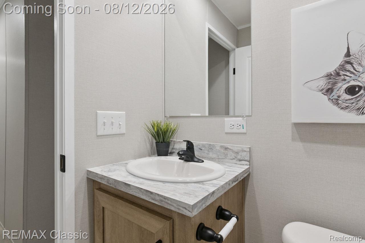 7105 West Vienna Road Clio, MI 48420 - Photo 11 of 23 Wood-finish vanity with a drop-in sink, stone-finish countertop, and wall-mounted mirror