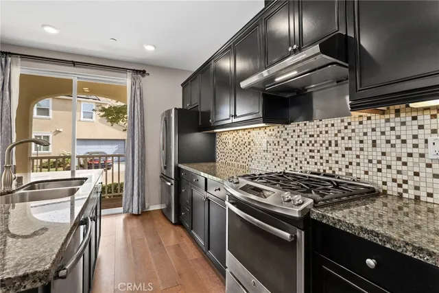 a kitchen with granite countertop a stove a sink dishwasher a refrigerator and wooden floor