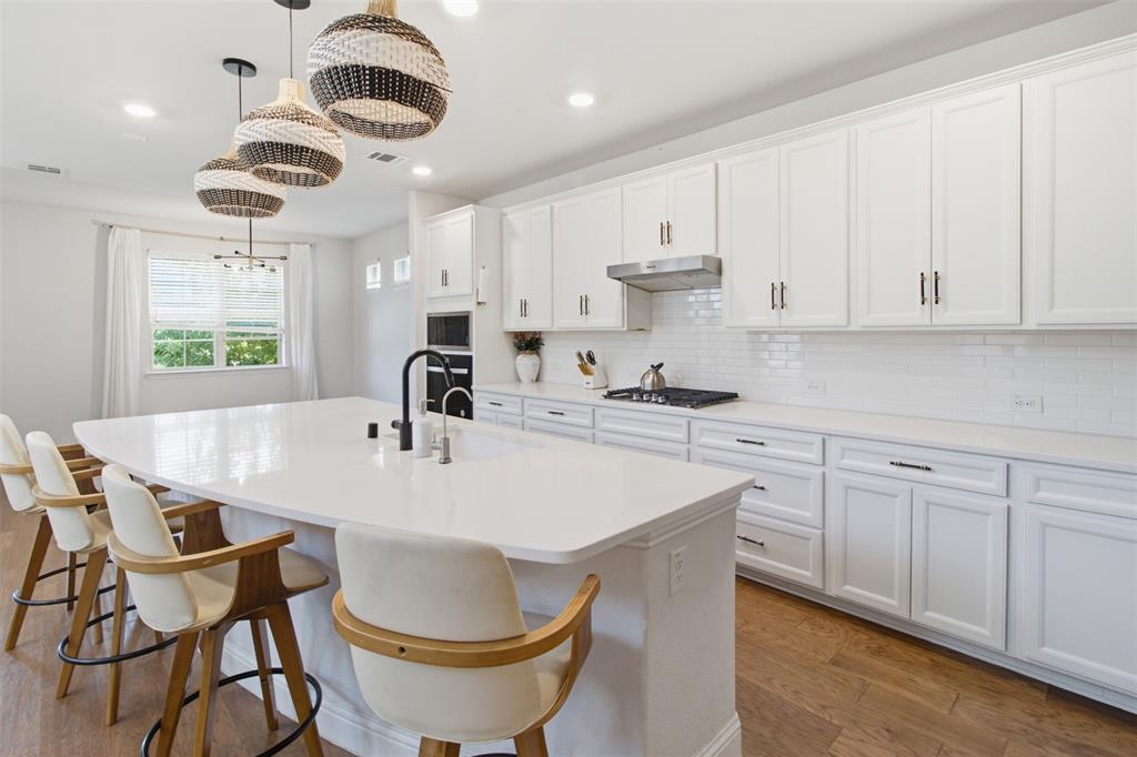 7416 Sequoia Rdg Road Little Elm, TX 76227 - Photo 21 of 37 Spacious kitchen featuring an oversized island with countertop seating, white shaker-style cabinetry, a subway tile backsplash, a built-in range, and wood-finish flooring