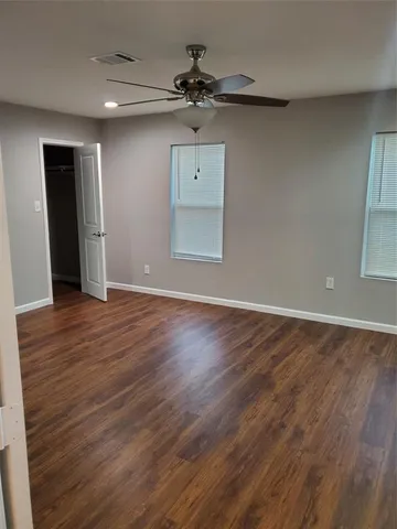 an empty room with wooden floor a ceiling fan and windows