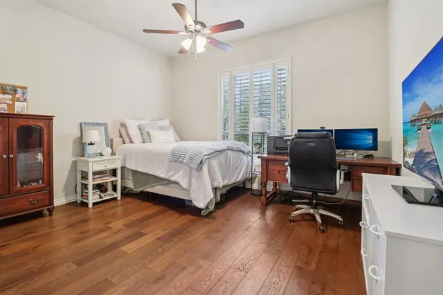 a bedroom with a bed a computer on a desk and wooden floor