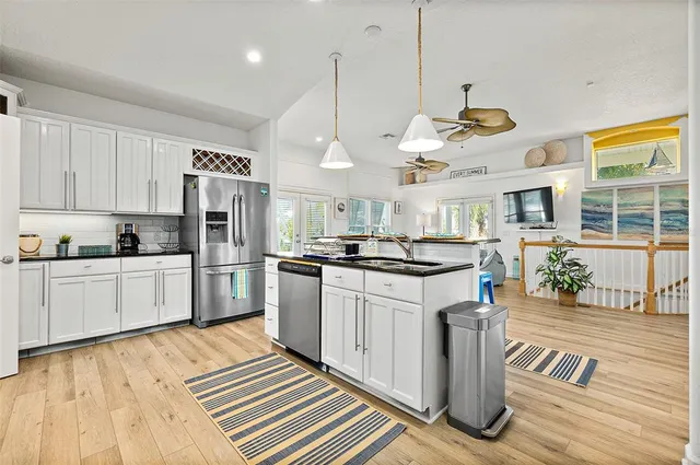 a kitchen with stainless steel appliances granite countertop a refrigerator a sink dishwasher a stove and white cabinets with wooden floor