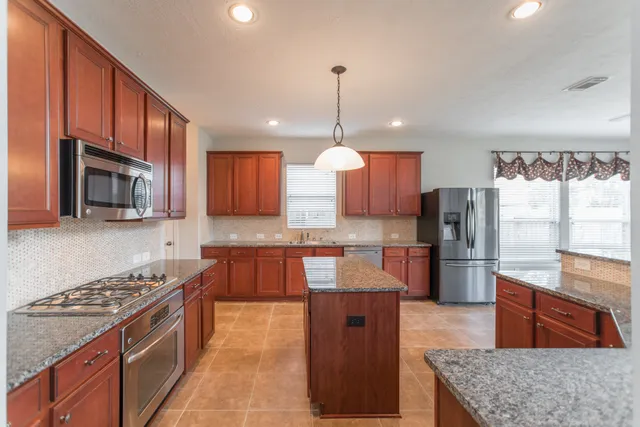 a large kitchen with stainless steel appliances granite countertop a stove a sink dishwasher a refrigerator and a microwave oven