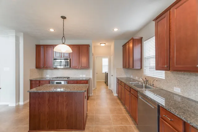 a large kitchen with stainless steel appliances granite countertop wooden cabinets a sink dishwasher a stove and a refrigerator with wooden floor
