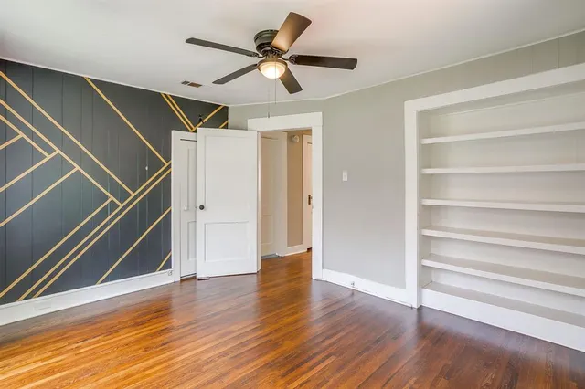 a view of an empty room with wooden floor and a ceiling fan