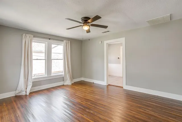 an empty room with wooden floor a ceiling fan and windows