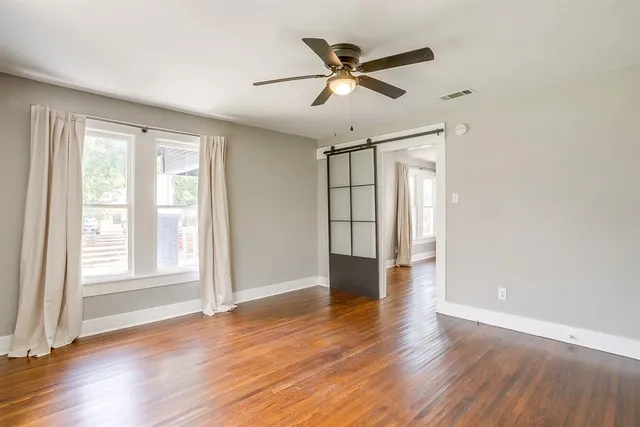 an empty room with wooden floor fan and windows