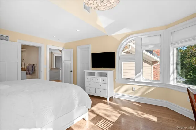 a spacious bedroom with a large bed and flat tv screen on dresser next to a window