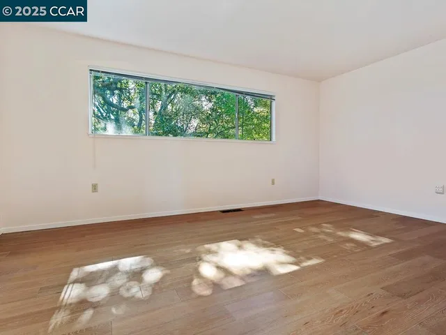 a view of an empty room with wooden floor and a window