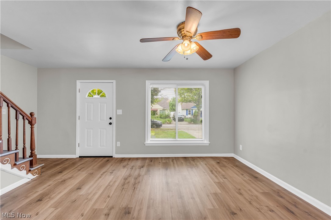 18517 Homeway Road Cleveland, OH 44135 - Photo 3 of 29 Open-concept room featuring wood-finish flooring, light gray walls, a white paneled entry door with an arched glass insert, a ceiling fan with light fixture, and a white-framed window