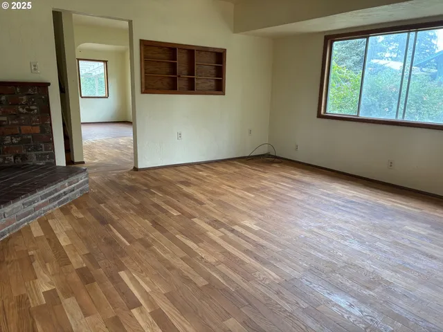 a view of an empty room with window and wooden floor