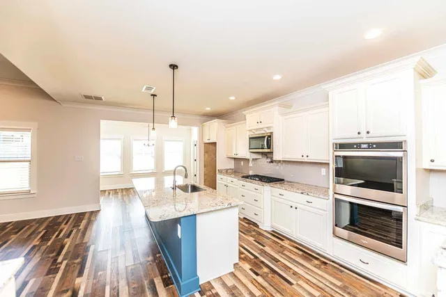 a kitchen with stainless steel appliances kitchen island granite countertop a stove a sink and white cabinets with wooden floor