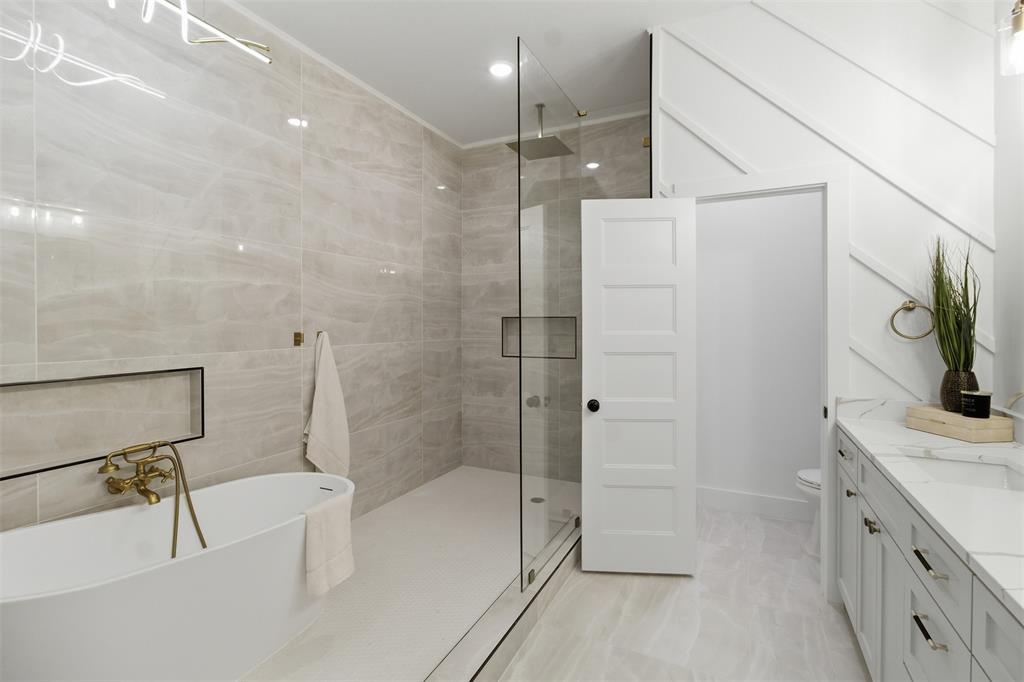 435 Waterboard Road Trinidad, TX 75163 - Photo 33 of 39 Spacious bathroom featuring a freestanding soaking tub with brass fixtures, a glass-enclosed shower with tiled walls and a recessed niche, a double vanity with a marble-finish countertop, and a decorative accent wall