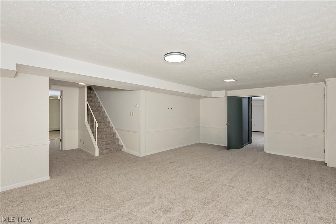 3189 Lander Road Pepper Pike, OH 44124 - Photo 38 of 43 Open lower-level room featuring light gray carpeting, white painted walls with chair rail molding, a neutral staircase with white railings, and recessed lighting