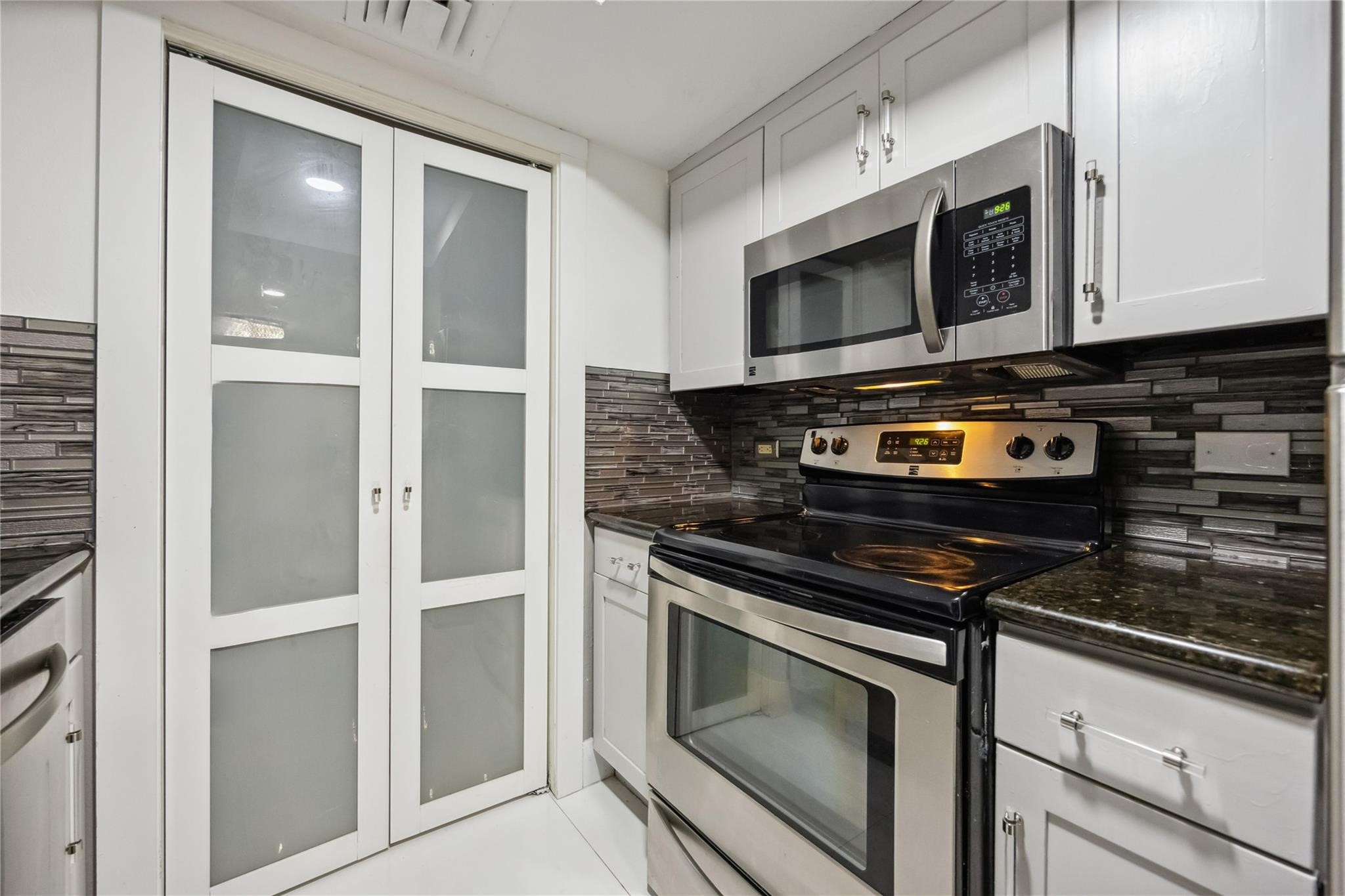 3525 Sage Road, Unit 1713 Houston, TX 77056 - Photo 22 of 25 This modern kitchen features stainless steel appliances, including a microwave and electric range, set against sleek dark countertops and a stylish tile backsplash.