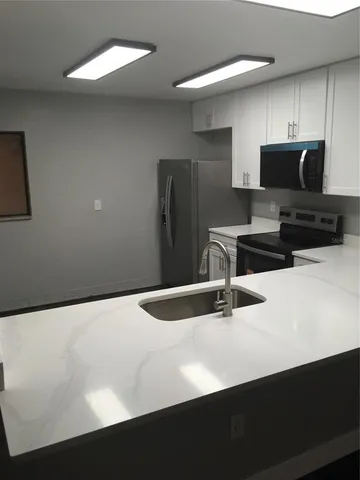 a kitchen with stainless steel appliances a sink a microwave a refrigerator and white cabinets