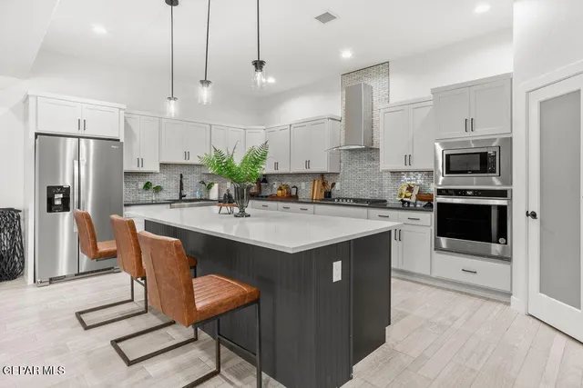 a kitchen with stainless steel appliances kitchen island granite countertop a sink a stove a refrigerator cabinets and chairs