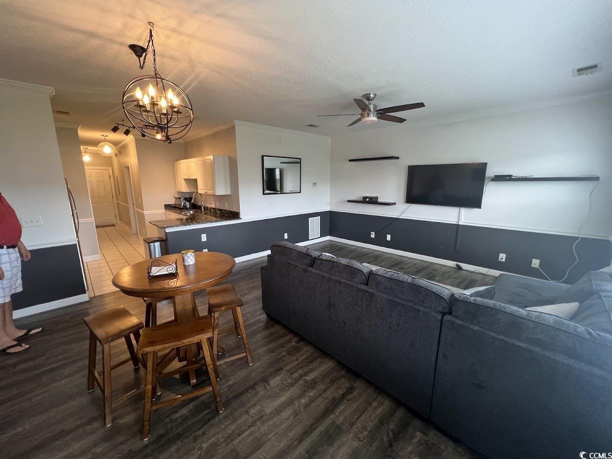 3965 Forsythia Court, Unit 202 Myrtle Beach, SC 29588 - Photo 5 of 15 Living area featuring a ceiling fan, dark wood-style flooring, a textured ceiling, a chandelier, and crown molding
