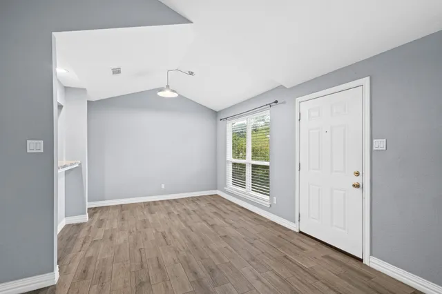a view of an empty room with wooden floor and a window