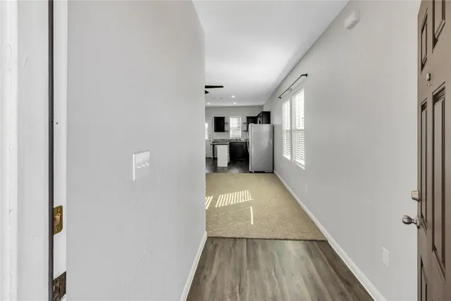 a view of a hallway to an empty room with wooden floor and a window