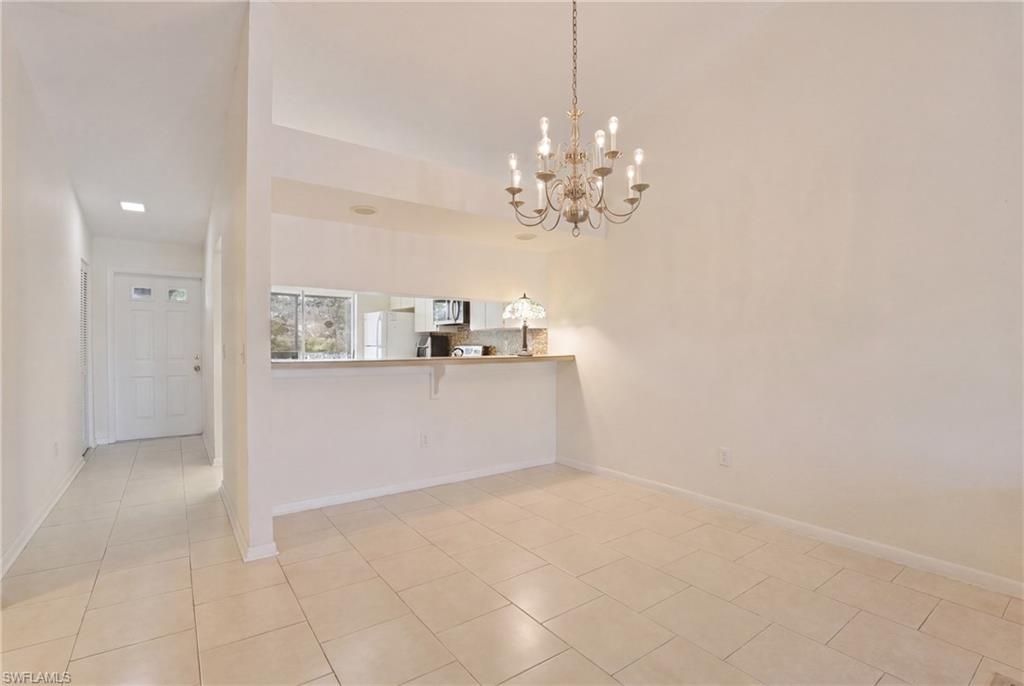 4050 Ice Castle Way, Unit 2812 Naples, FL 34112 - Photo 12 of 49 Open-concept dining area featuring a multi-bulb chandelier, tile flooring, and a pass-through counter to the kitchen