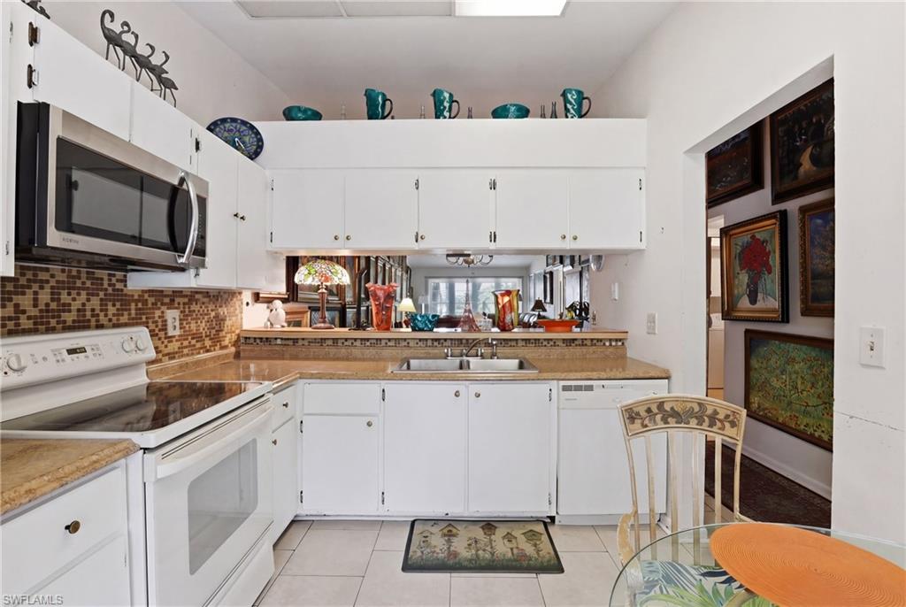 4050 Ice Castle Way, Unit 2812 Naples, FL 34112 - Photo 7 of 49 Kitchen featuring white cabinetry, a stainless steel microwave, a glass cooktop range, a tile backsplash, and light-toned countertops