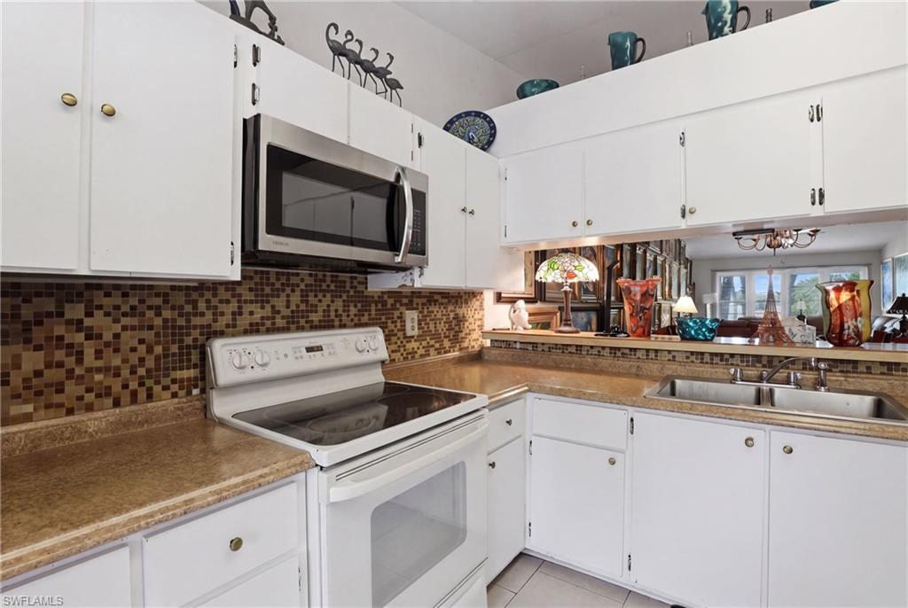 4050 Ice Castle Way, Unit 2812 Naples, FL 34112 - Photo 10 of 49 Kitchen featuring white cabinetry, a stainless steel over-the-range microwave, a white electric range, mosaic tile backsplash, and a double basin sink