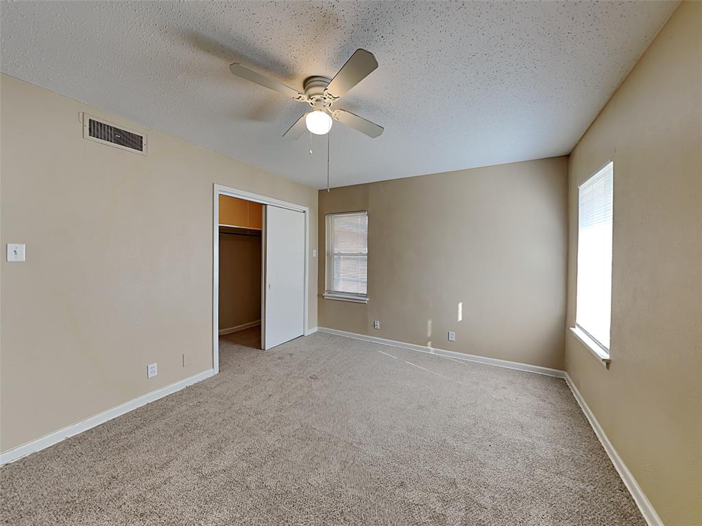 649 West Main Street Lancaster, TX 75146 - Photo 4 of 14 Unfurnished bedroom with a textured ceiling, ceiling fan, multiple windows, light colored carpet, and a spacious closet