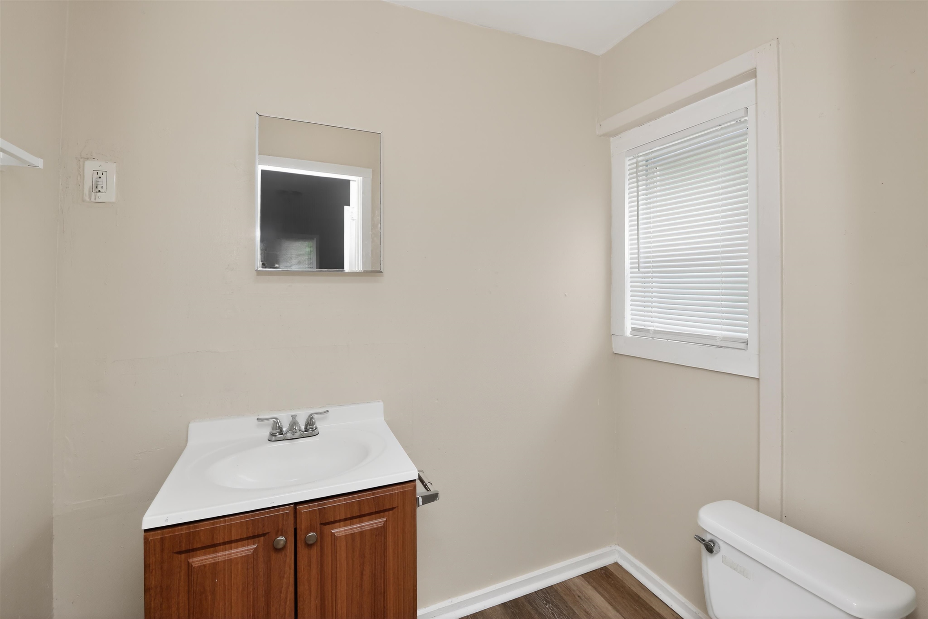 4838 Manson Road Memphis, TN 38109 - Photo 27 of 28 Bathroom featuring wood-finish flooring, a rectangular window with blinds, a white vanity with a single basin sink, and a wall-mounted mirror