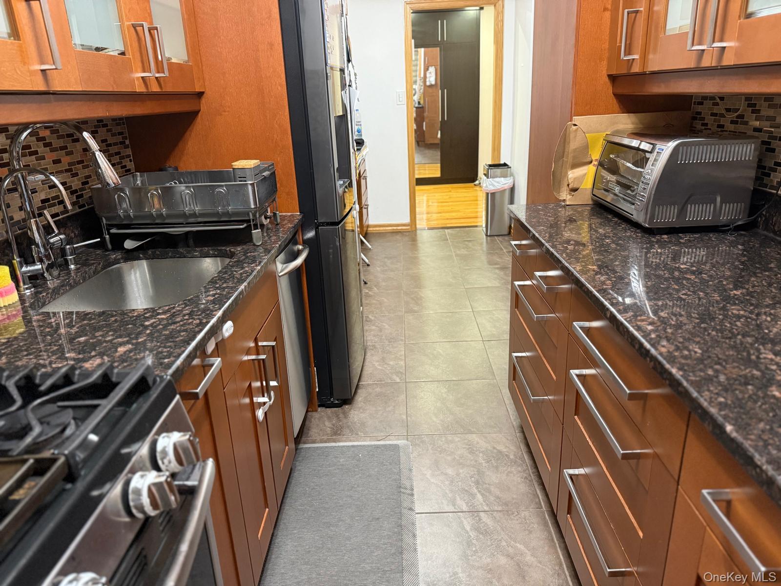 105-25 65th Avenue, Unit 5H Queens, NY 11375 - Photo 3 of 6 Kitchen with decorative backsplash, brown cabinets, and stainless steel appliances