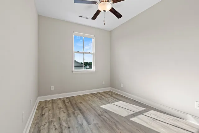 an empty room with wooden floor chandelier fan and windows