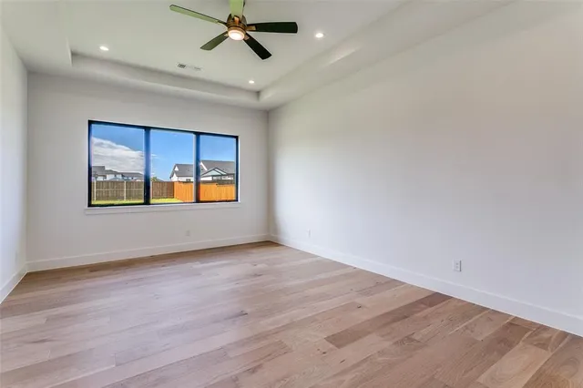 an empty room with wooden floor ceiling fan and windows
