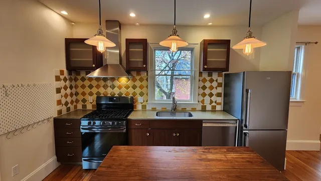 a kitchen with stainless steel appliances kitchen island granite countertop a stove a refrigerator and a wooden floors