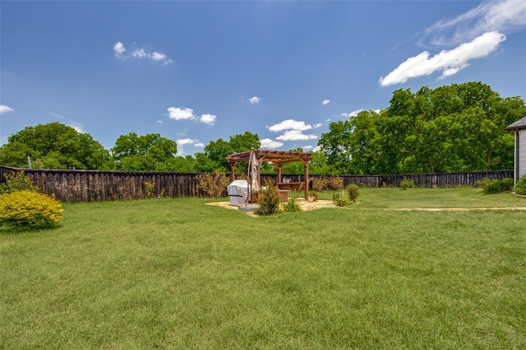1105 Ranch Drive Bonham, TX 75418 - Photo 25 of 25 Expansive grassy backyard featuring a wooden pergola on a light-colored patio, mature privacy fencing, and established perimeter trees