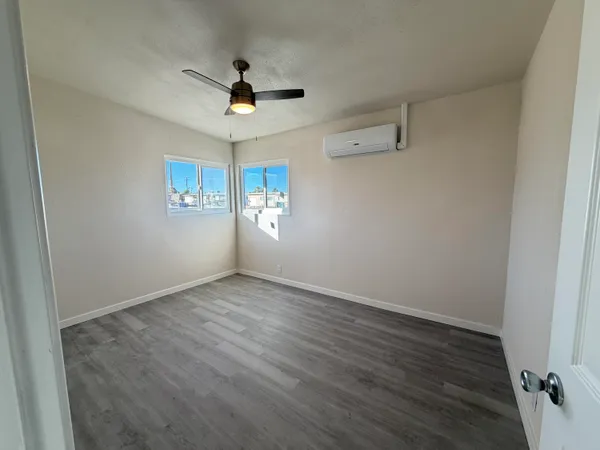 an empty room with wooden floor chandelier fan and windows